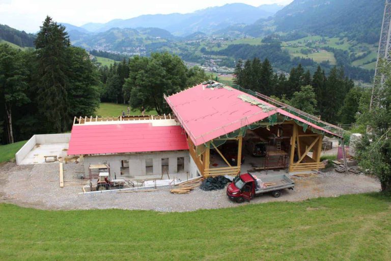 Blick auf den neugebauten Maurachhof mit rotem Dach und umgebender Berglandschaft.