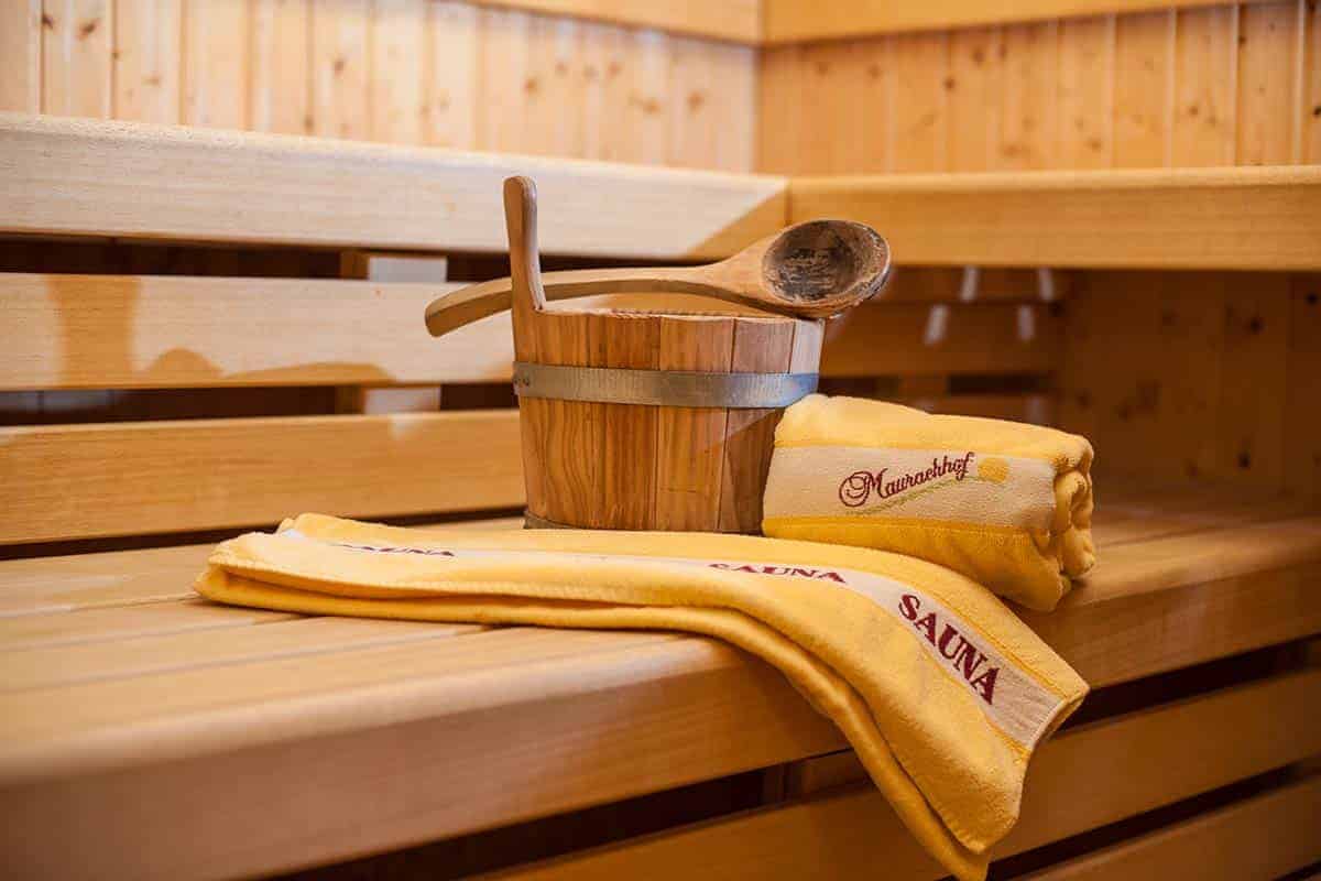 Holzsauna mit Saunabezubehör, Handtüchern und Holzeimer für Entspannung am Bauernhof.