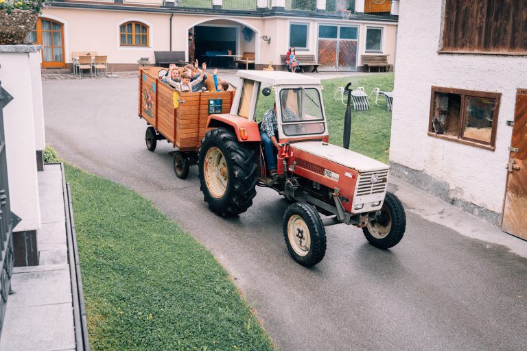Traktor mit Anhänger voller fröhlicher Kinder auf Bauernhofhofweg