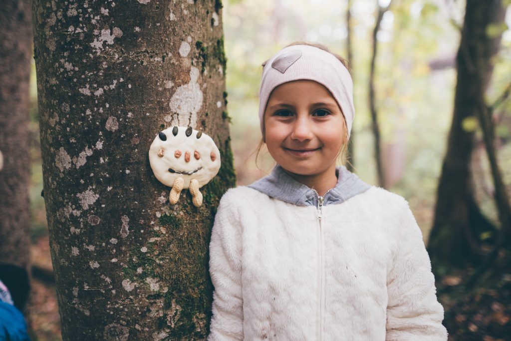 Girl in the forest next to a tree with a funny face made of natural materials